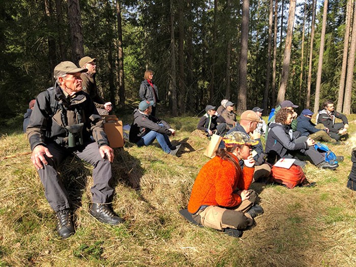 Människor står och sitter på exkursion i skogen. Foto.
