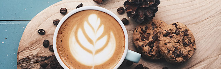 Kaffe på en skärbräda med kakor och kaffebönor bredvid. Foto. 