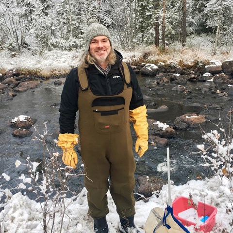 Man in waders in fron of wintery stream. Photo.