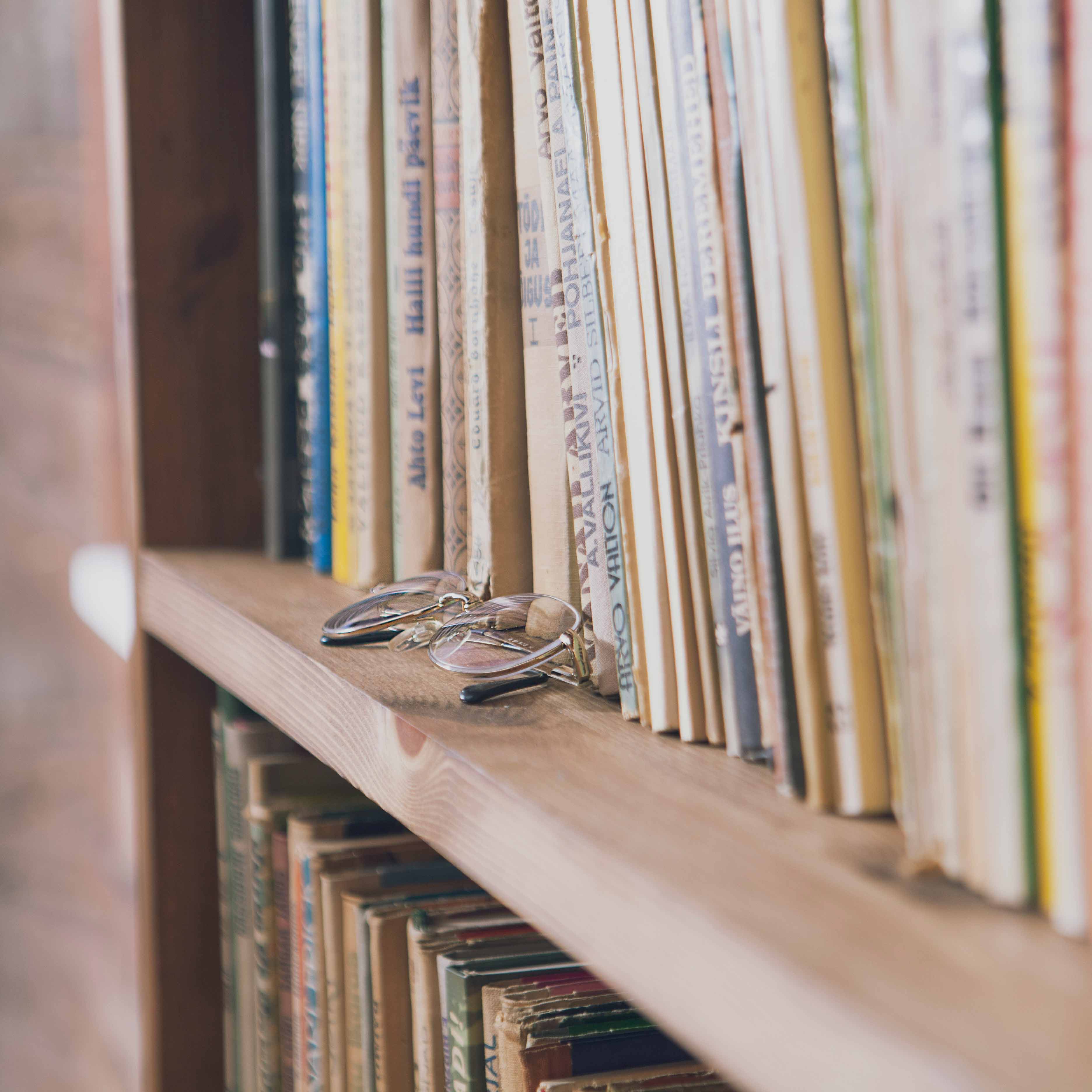 Närbild på en bokhylla med ett par glasögon på kanten av hyllan. 