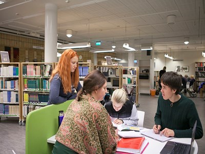 Fyra studenter samtalar runt en grupparbetsplats i ett bibliotek