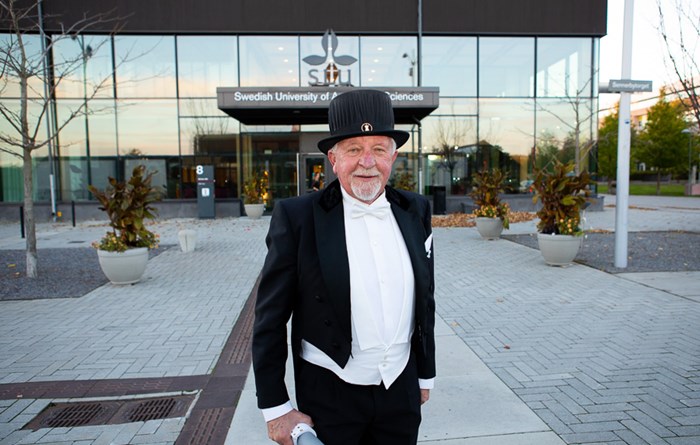 Honorary doctor Rune Andersson wearing his doctor's hat in front of the main entrance of SLU in Uppsala.