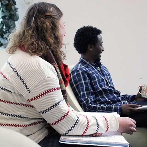 Man and woman, seemingly of African and European backgrounds, laugh at a seminar. Photo.