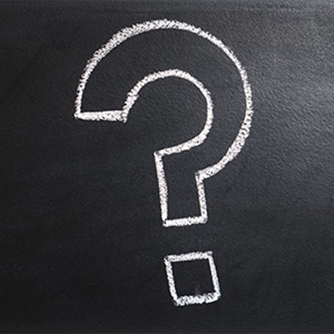 Thick question mark written with white chalk on blackboard. Photo.