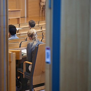 Through half open door, students in lecture hall are shown. Photo.