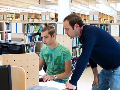 Två studenter framför en dator i biblioteket, foto.