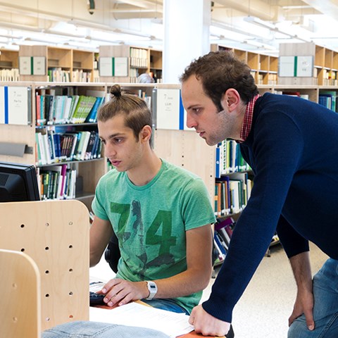 Two students in front of a computer in the library, photo.