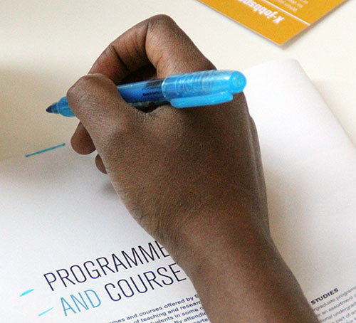 Close-up of a student holding a pen and looking at SLU's programme catalog, photo.