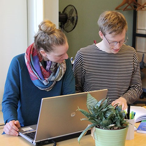 Two students sitting at a desk with a laptop and notebooks, photo.