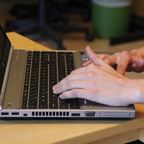 Närbild på en persons händer och en laptop, foto.