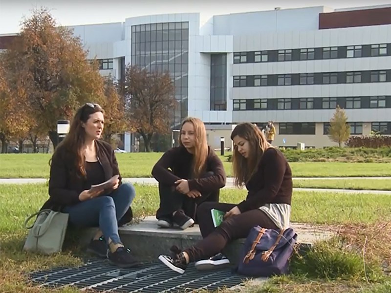 Tre studenter sitter utanför en campusbyggnad, foto.