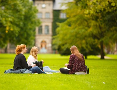 Tre kvinnliga studenter sitter på gräsmattan i Alnarsparken, foto.