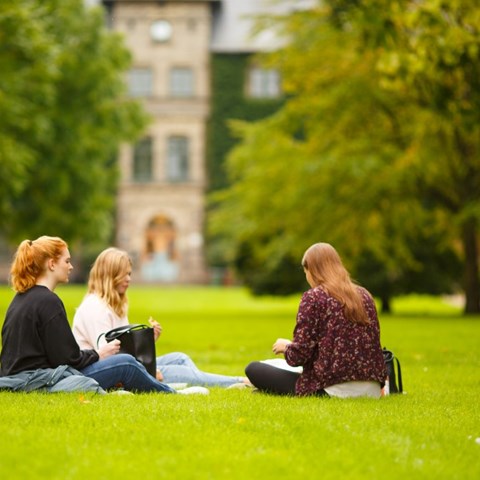 Tre kvinnliga studenter sitter på gräsmattan i Alnarsparken, foto.