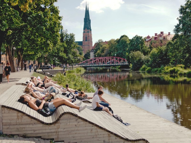 People sit along Fyrisån in Uppsala, photo.