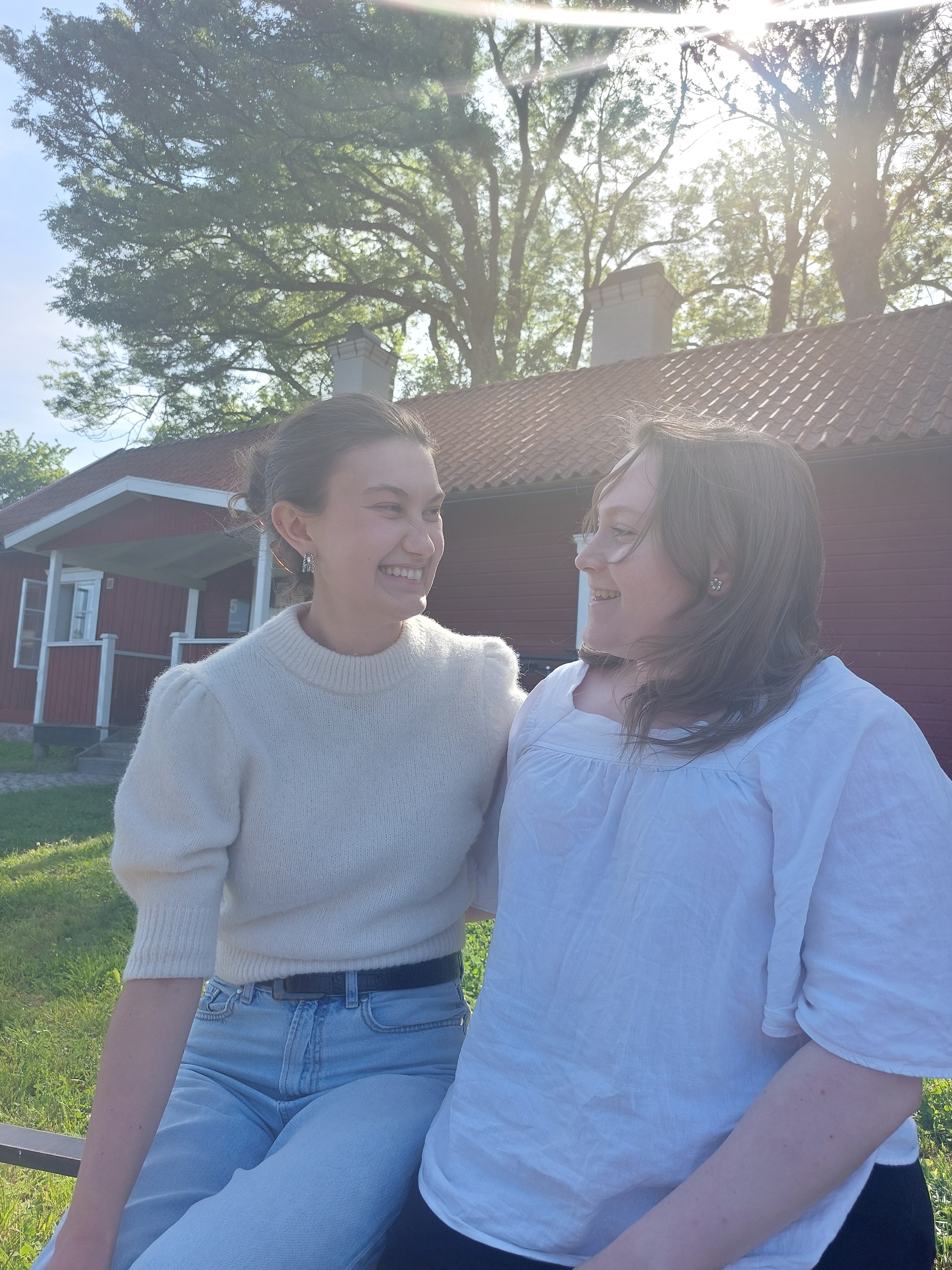 Tova and Tilde sharing a sunny moment in front of the red cottage.